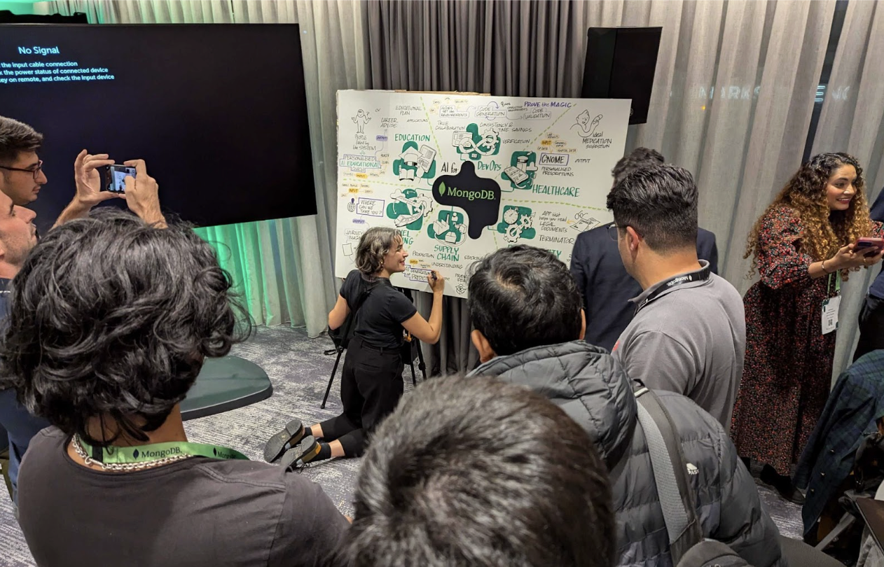 Photograph of graphic recorder Maria Foulquie putting the final touches on an illustration. She is kneeling on the ground drawing on a big board with a crowd around her watching.